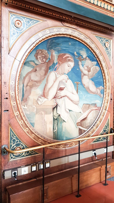 Photo 2 of Biblioteque Genevieve interior, showing a circular wall mural of a lady and two cherubs. The mural has a decorative wooden border around it.