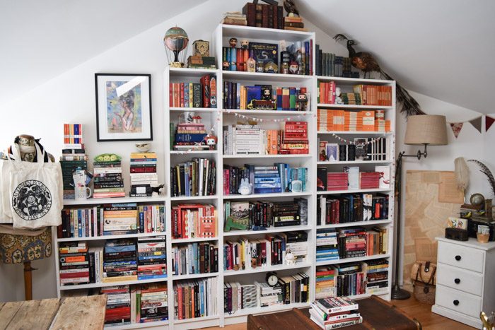 How to Organise Your Bookshelves - Room with white bookshelves of various sizes and heights filled with colourful books and trinkets.