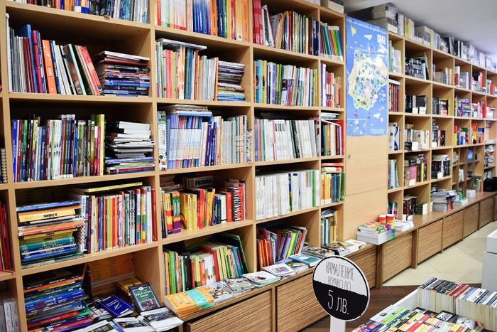 Interior of Сolibri Publishers, bookstore in Sofia, Bulgaria. Wooden bookshelves and a low table are filled with neatly stacked books.