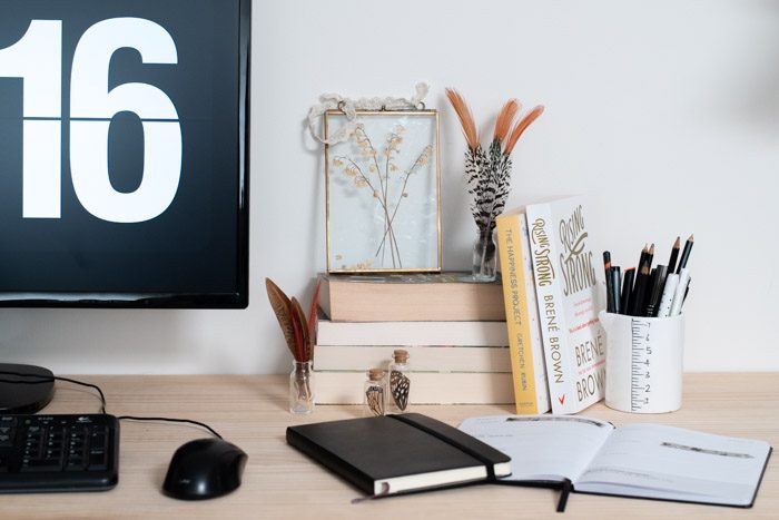 4 Ways to Care for Yourself as a Creative. Images shows a desk with computer, stack of books, open journal and stationary in a jar