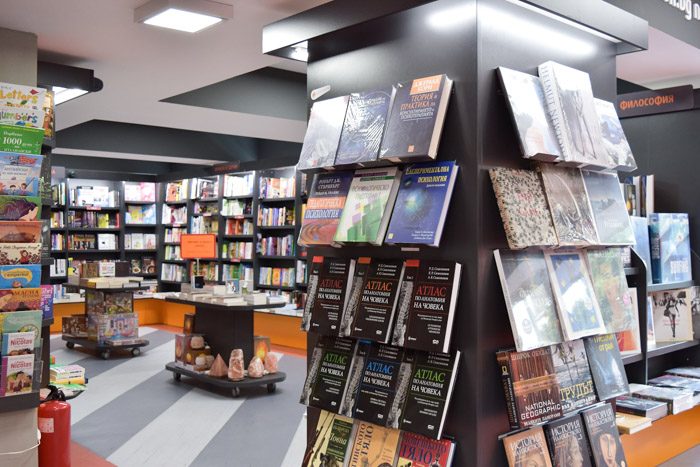 Interior of Helicon Books, bookstore in Sofia, Bulgaria. Black bookshelves and small tables are filled with neatly stacked books.