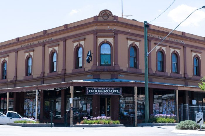 Exterior of Stoneman's Book Room in Castlemaine Victoria, a large old building painted brown with burgundy trim. Under a covered veranda a window display of books is visible.