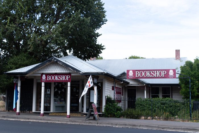 Exterior of Aesop's Attic Bookshop, Woodend. A white cottage style house with a grey tin roof. Two maroon signs say 'Bookshop'.