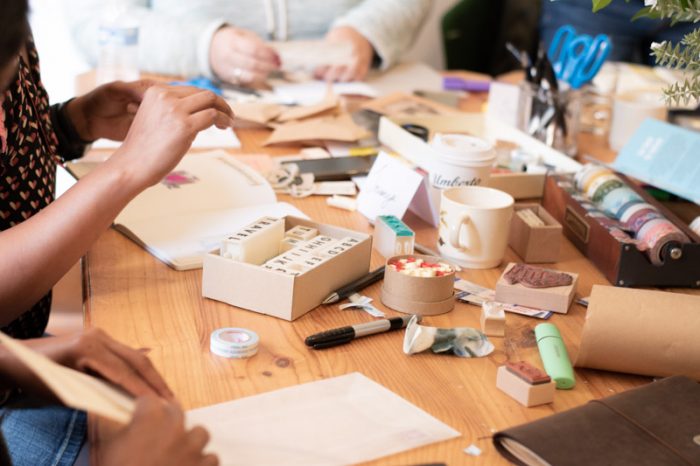 Creative Journaling Workshop Melbourne. A table filled with stamps, paper and supplies and the hands of three people working on creative journals