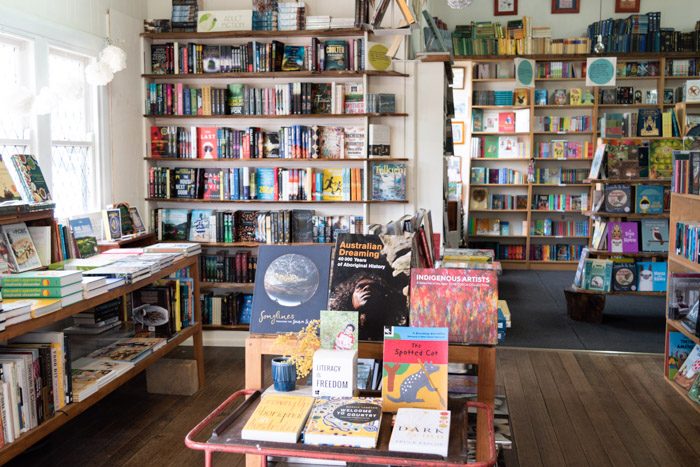 Interior of New Leaves. A bright, open bookstore with neat shelves on all walls and windows on the left. A display in the foreground on a table features books by Aboriginal authors.