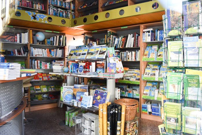 Inside Anavasi, Athens, Greece. A small crowded shop is visible, maps and guide books are visible on every surface.