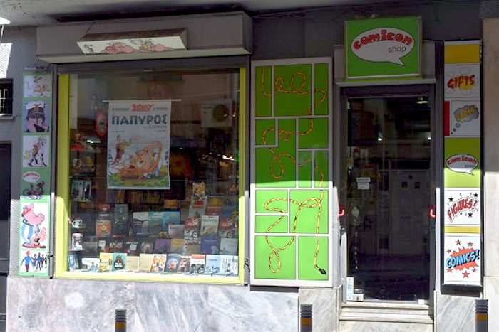 Front of Comicon, Athens, Greece. Vivid lime green signs decorate the shop front. The window display has various comic books.