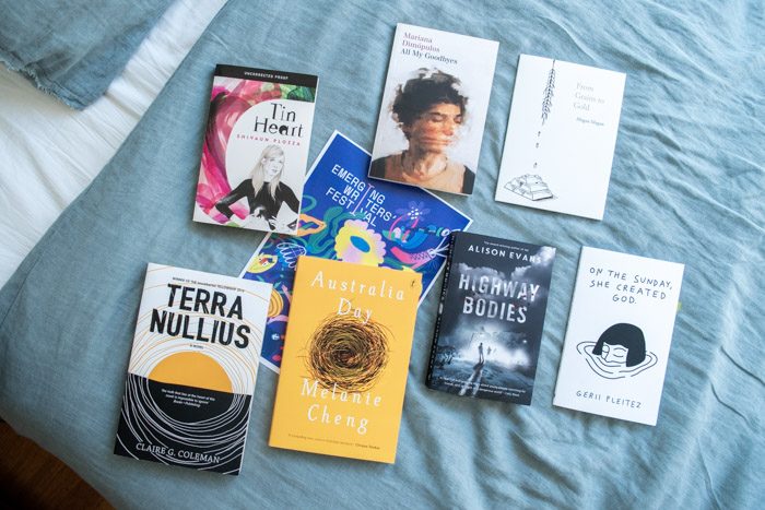 Books from Emerging Writer's Festival 2019, lying face up on a bed with pale blue sheets. The titles are: Tin Heart, From Grains to Gold, All My Goodbyes, On The Sunday She Created God, Highway Bodies, Australia Day, Terra Nullius.