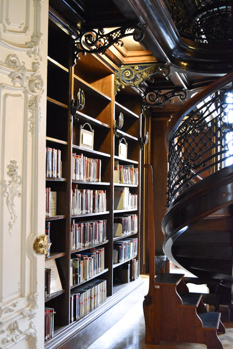 The interior of the Metropolitan library, displaying part of the spiral staircase and a range of antique books on sturdy wooden bookshelves.