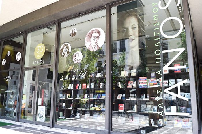 Front of Ianos Art, Athens, Greece. The largest shopfront of all the shops in this post, huge glass windows and double glass doors are decorated with circular decals of famous authors. Oscar Wilde is the most easily recognisable. Inside large black bookshelves filled with books can be seen.