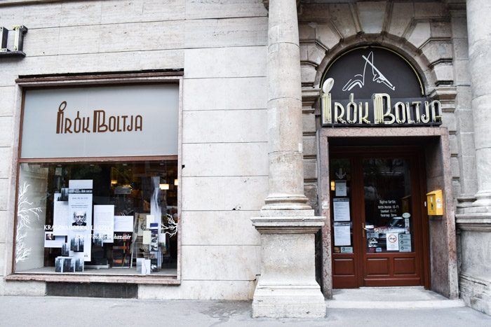 The front of this bookshop, with a heavy stone facade and art deco lettering above an inset wooden door.