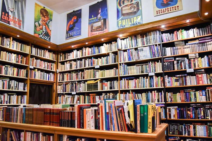 Inside Kozponti Antikvarium, with large well-lit bookshelves and vintage posters above them.