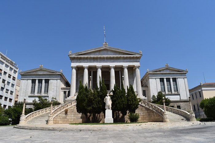 Front of the National Library of Greece, and imposing building with six columns supporting a peaked roof and a curved staircase leading to the front.