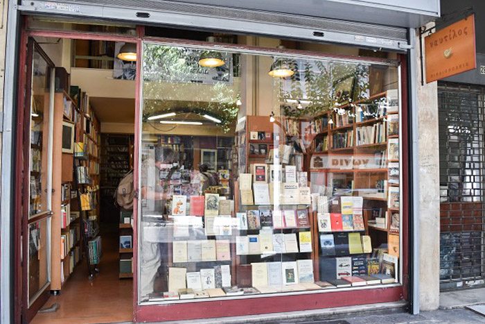 Front of Nautilus Bookstore, Athens, Greece. A large square window reveals a display of books. An open doorway to the left shows wooden bookcases.