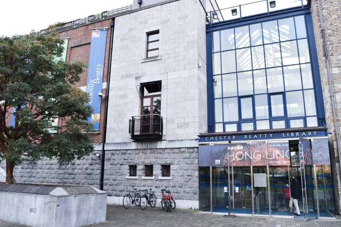 A large building made from a number of different coloured materials, such as red brick, pale stone, and framed glass. A sign on the front says Chester Beatty Library.