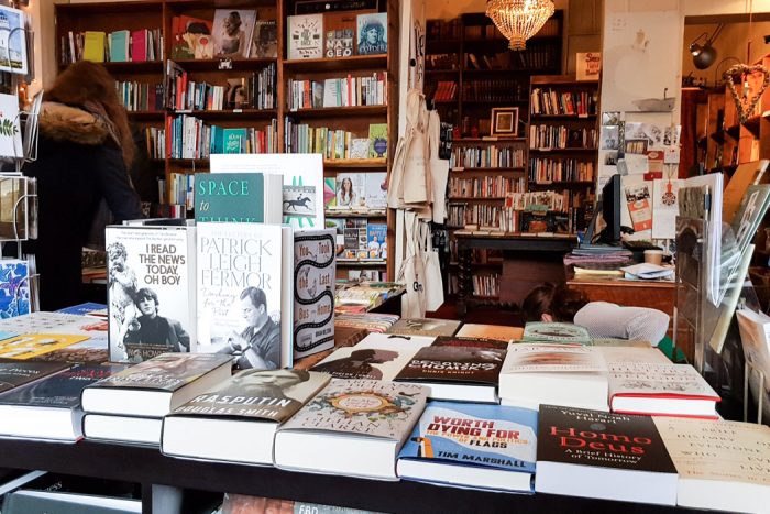 Table stacked with all kinds of books and surrounded by other bookshelves