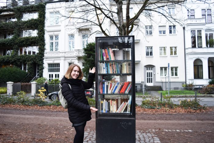 Young woman standing next to a cabinet filled with books on the pavement in the city of Bonn