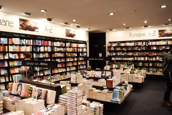 One corner of a bookshop with lots of books for sale on the walls and display tables.