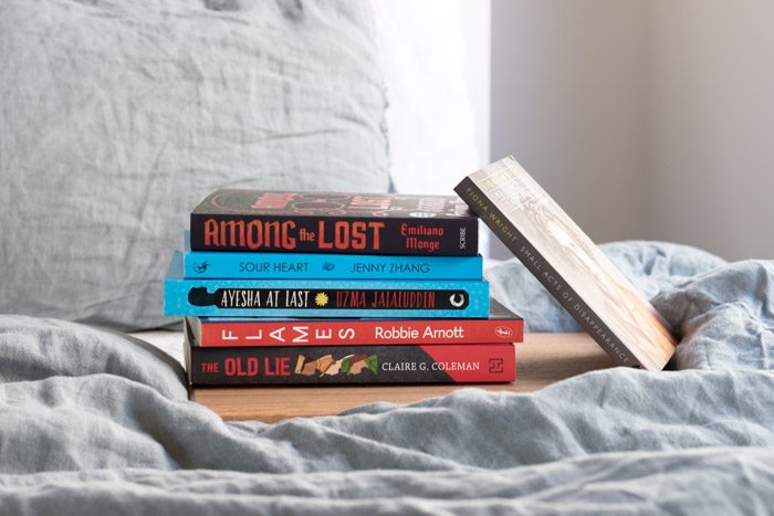 7 Books to Read from Ubud Writers and Readers Festival - Stack of 6 books on a bed with pale blue linen. 