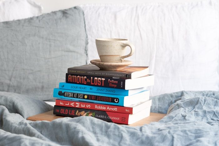 7 Books to Read from Ubud Writers and Readers Festival - Stack of 6 books on a bed with pale blue linen. 