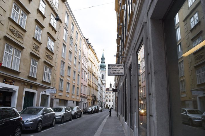 Gazing down a one way street in Vienna, with five-storey period buildings on either side, and cars parked on one side of the street.