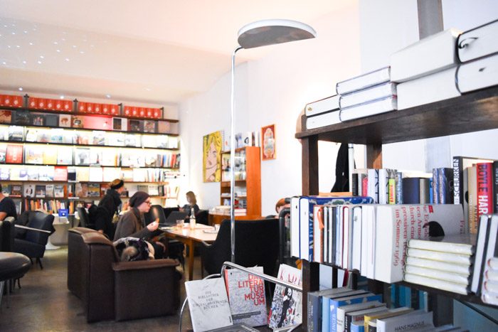 The interior of Phil, showing a few people sitting on low couches reading or talking, next to a set of grey, low bookshelves.