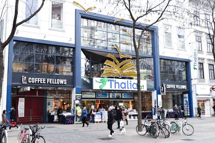 A modern glass 3-storey shopfront, with the shop name (Thalia) in big blue letters on a white background, along with a large decorative 3D image of a book just above it. 