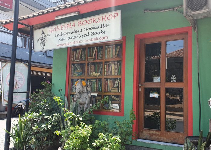 Exterior of Ganesha Bookshop in Ubud, Bali, Indonesia. A small green building with red painted edges around the door and a fake window with books painted on it.