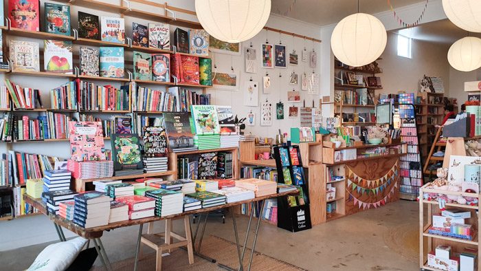 Interior of Squishy Minnie Bookstore in Kyneton. A colourful range of books are displayed on shelves and tables and the counter is decorated with rainbow bunting.