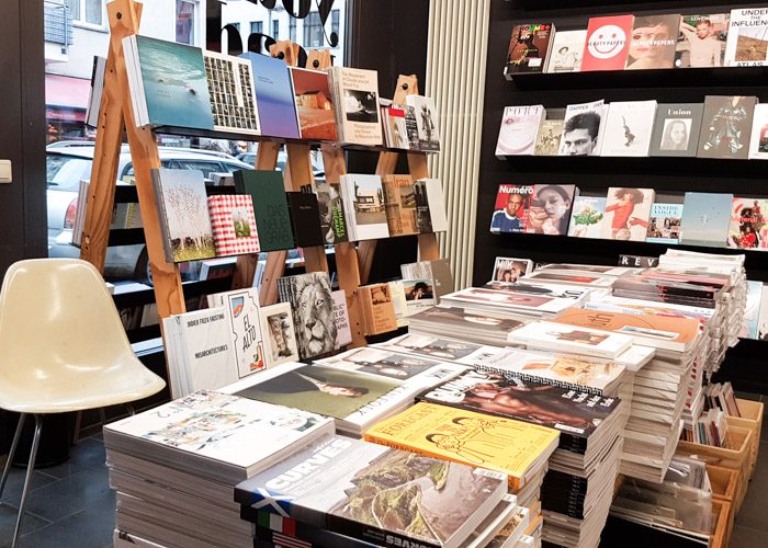 Two easels used as bookshelves behind a table stacked with a very large amount of large coffee table books in Do You Read Me bookshop.