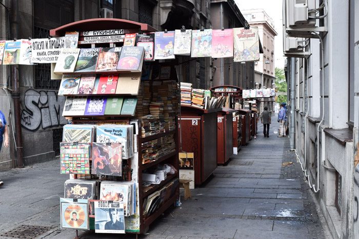 Book Cart Street, Ulica Hiljadutrista Kaplara, carts are piled with old books along a narrow laneway between old buildings. Book Lover's Guide to Belgrade, Serbia.