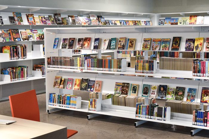 Geelong Library interior, long white shelves are stacked neatly with books. A red chair is visible in the foreground.