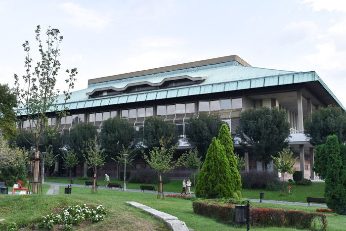 Exterior of the National Library of Serbia. Large building with a green roof is visible behind trees in a park. Book Lover's Guide to Belgrade, Serbia.