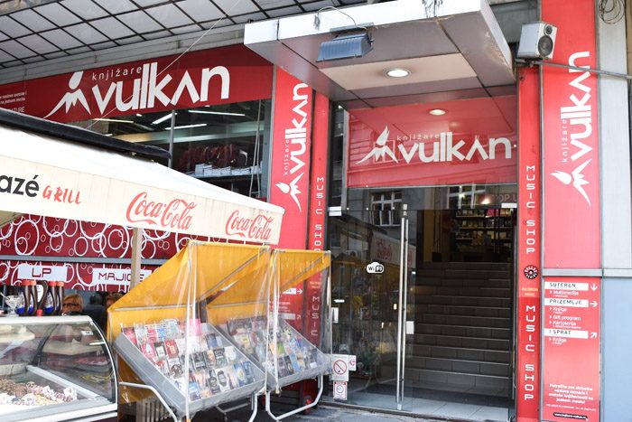 Exterior of Vulcan book store chain. Red signs with the Vulkan name are plastered around the windows and above the door. Book Lover's Guide to Belgrade, Serbia.